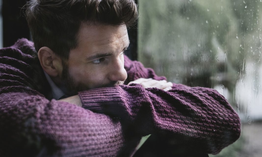 young-man-arms-folded-over-knees-at-window